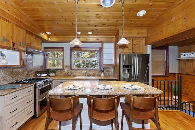 kitchen featuring sink, light stone counters, pendant lighting, stainless steel appliances, and white cabinets