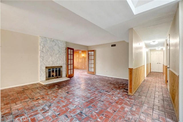 unfurnished living room featuring wood walls, a fireplace, and french doors