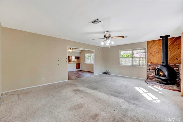 unfurnished living room featuring a wood stove, ceiling fan, and carpet flooring