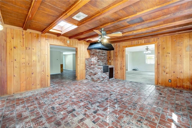 unfurnished living room featuring wooden walls, a skylight, ceiling fan, wooden ceiling, and beam ceiling