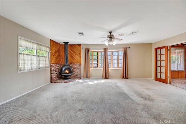 unfurnished living room featuring plenty of natural light, carpet flooring, and a wood stove