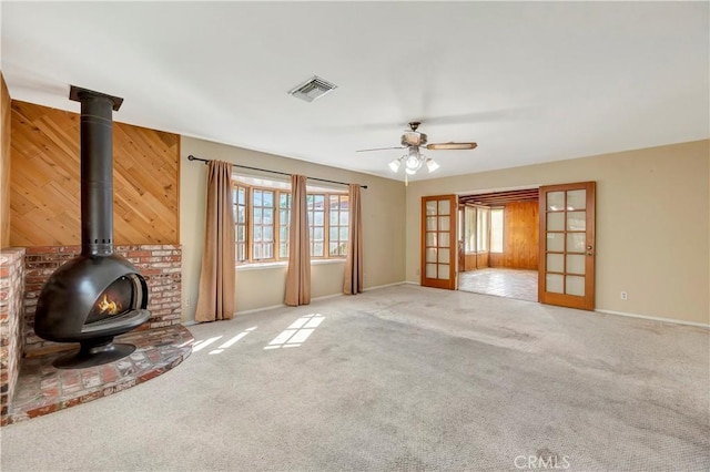 unfurnished living room with light colored carpet, french doors, ceiling fan, and a wood stove