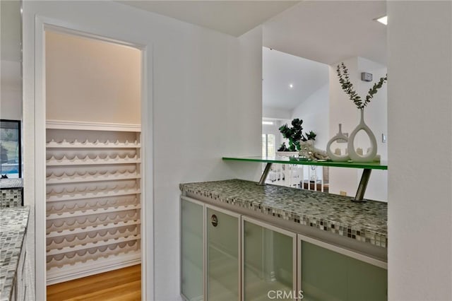 bar featuring light stone counters, vaulted ceiling, green cabinets, and light wood-type flooring