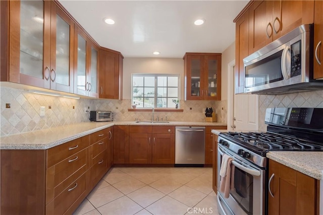 kitchen with sink, light tile patterned floors, appliances with stainless steel finishes, light stone countertops, and decorative backsplash