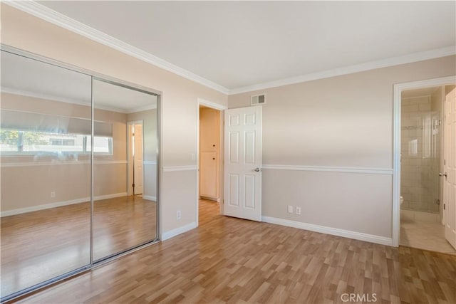 unfurnished bedroom with crown molding, connected bathroom, light hardwood / wood-style floors, and a closet