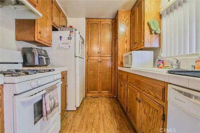 kitchen with white appliances, sink, tile countertops, and light hardwood / wood-style floors