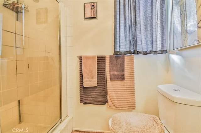 bathroom featuring a shower with door and toilet