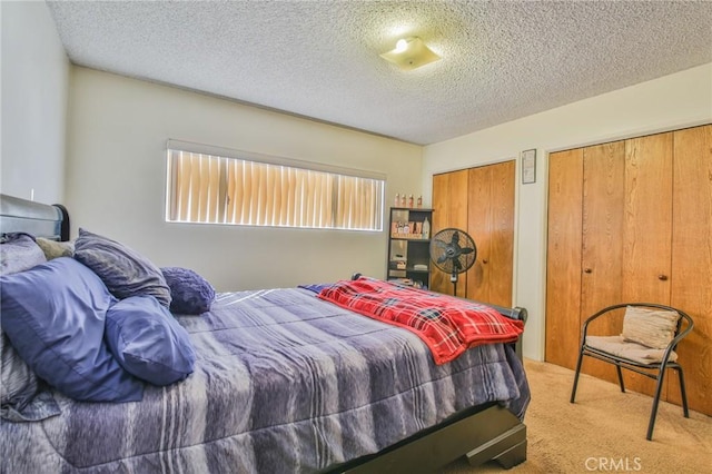 bedroom featuring light colored carpet, a textured ceiling, and two closets