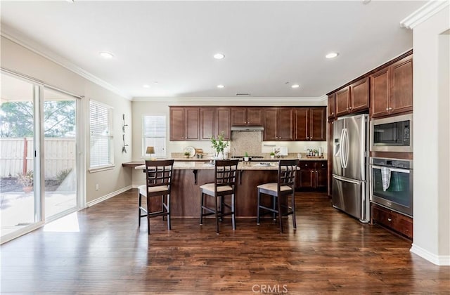 kitchen with crown molding, appliances with stainless steel finishes, a kitchen breakfast bar, a center island with sink, and dark hardwood / wood-style flooring