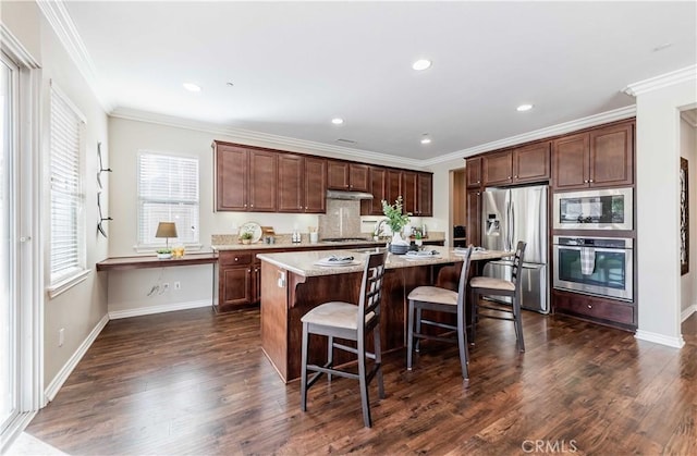 kitchen with dark hardwood / wood-style flooring, appliances with stainless steel finishes, a center island, and a kitchen bar