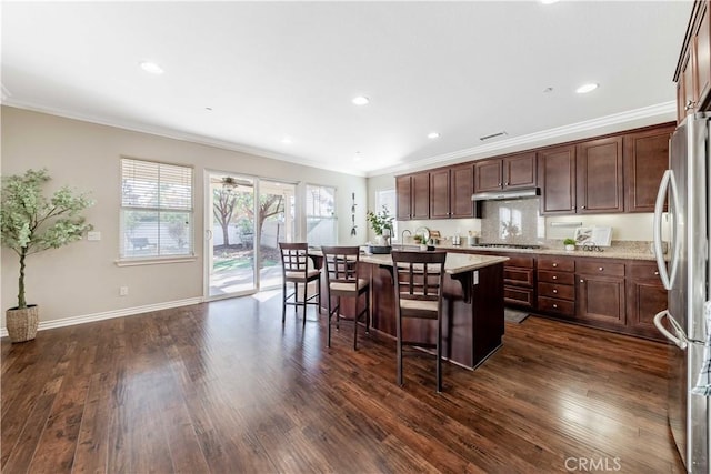 kitchen featuring stainless steel appliances, a kitchen breakfast bar, ornamental molding, a center island with sink, and dark hardwood / wood-style flooring