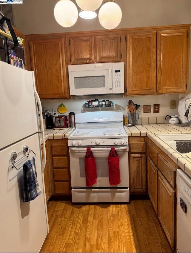 kitchen with tile counters, white appliances, and light hardwood / wood-style floors