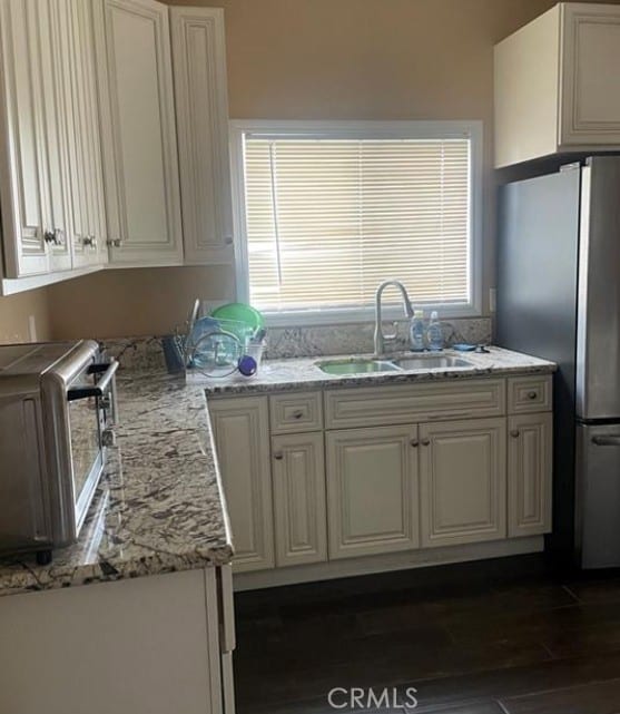 kitchen featuring dark wood-type flooring, sink, white cabinetry, stainless steel refrigerator, and light stone countertops