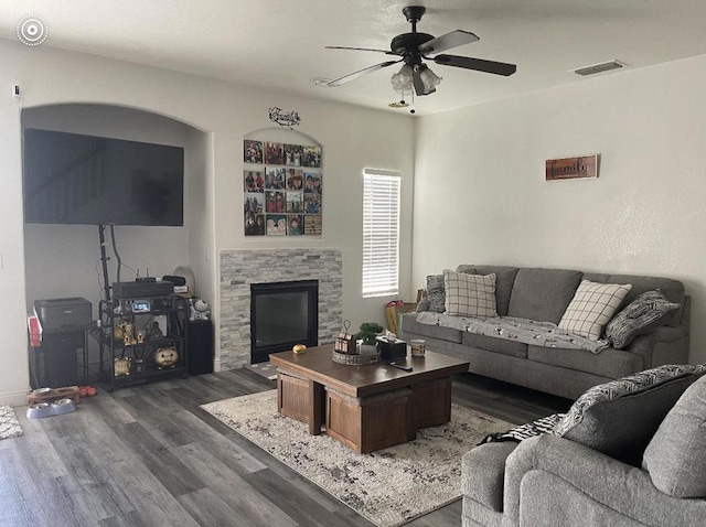 living room featuring ceiling fan, dark hardwood / wood-style flooring, and a stone fireplace