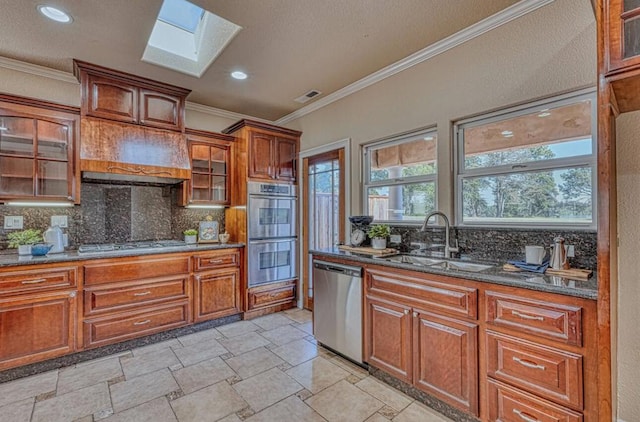 kitchen featuring sink, appliances with stainless steel finishes, a skylight, tasteful backsplash, and dark stone counters