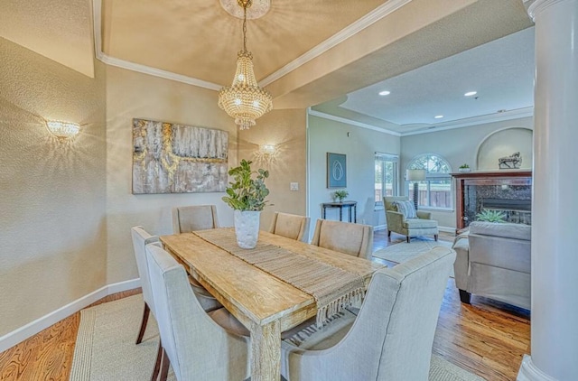 dining space with light hardwood / wood-style flooring, decorative columns, a notable chandelier, a tray ceiling, and ornamental molding