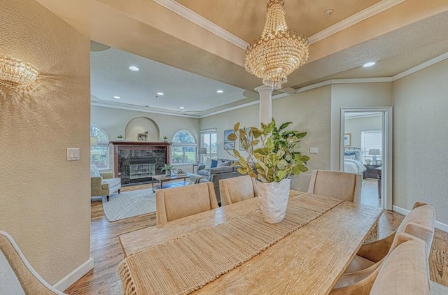 dining area with crown molding, a tray ceiling, a high end fireplace, a chandelier, and light wood-type flooring