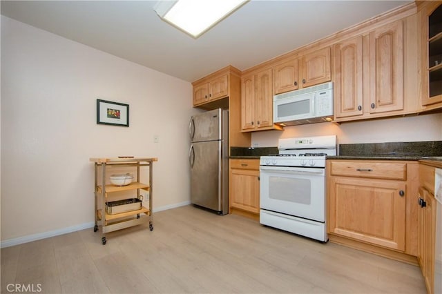 kitchen featuring white appliances, dark stone countertops, light brown cabinets, and light wood-type flooring