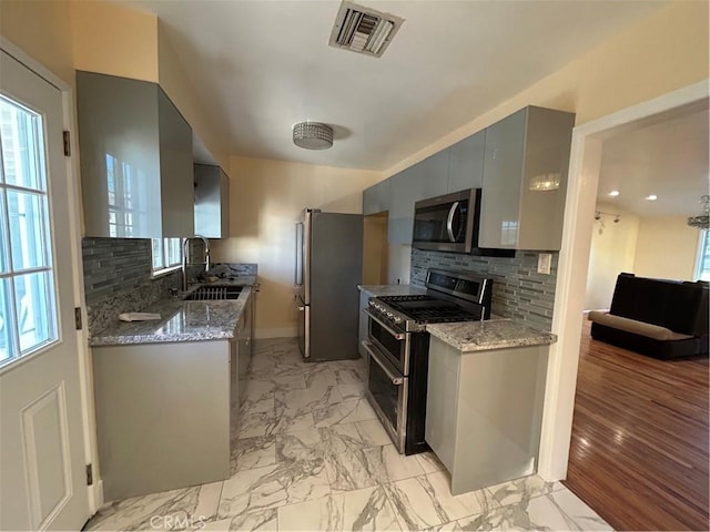 kitchen featuring appliances with stainless steel finishes, tasteful backsplash, sink, gray cabinetry, and light stone countertops