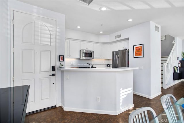 kitchen featuring decorative backsplash, kitchen peninsula, white cabinets, and appliances with stainless steel finishes