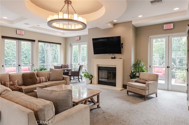 carpeted living room with french doors, plenty of natural light, and a raised ceiling