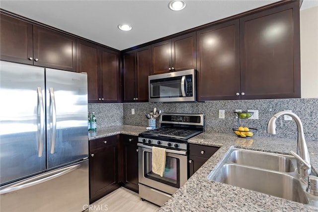 kitchen featuring appliances with stainless steel finishes, sink, decorative backsplash, light stone countertops, and dark brown cabinets