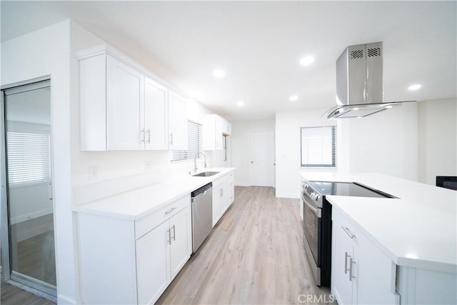 kitchen featuring appliances with stainless steel finishes, white cabinetry, sink, island exhaust hood, and light hardwood / wood-style flooring