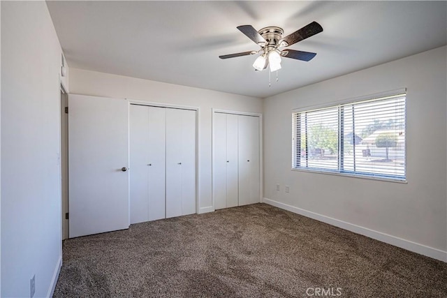 unfurnished bedroom with multiple closets, ceiling fan, and dark carpet