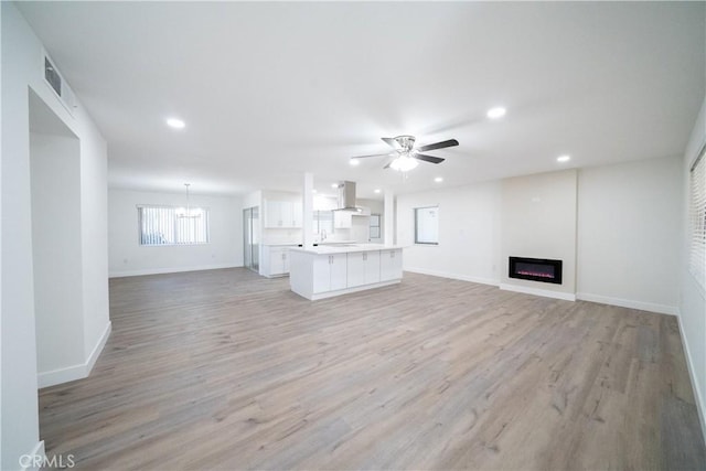 unfurnished living room featuring ceiling fan with notable chandelier and light hardwood / wood-style flooring