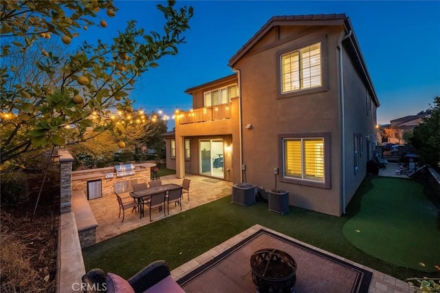 back house at dusk featuring a lawn, a patio, an outdoor fire pit, area for grilling, and a balcony