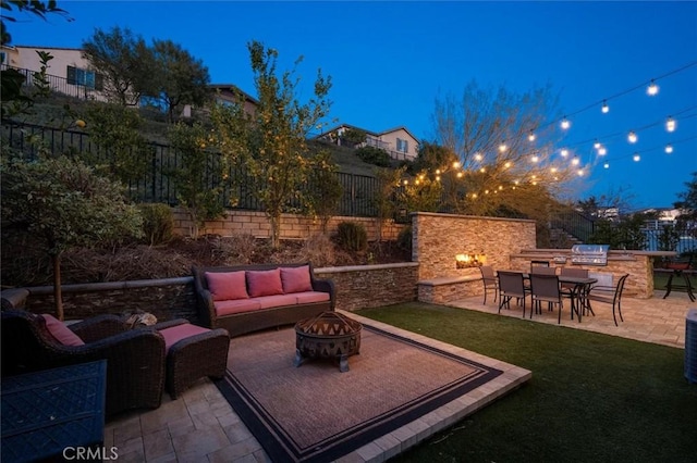 patio terrace at dusk featuring a yard, an outdoor living space with a fire pit, and exterior kitchen