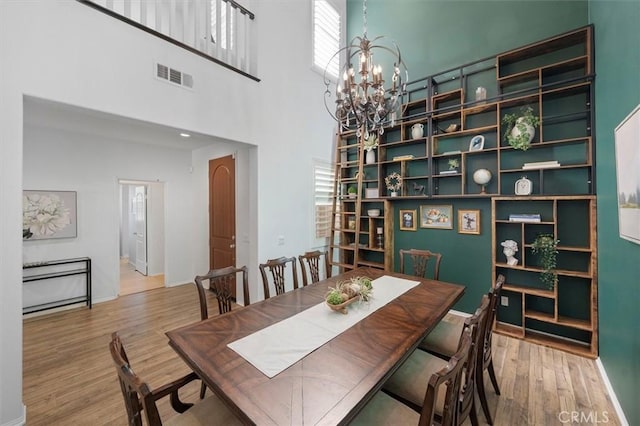 dining area featuring an inviting chandelier, hardwood / wood-style flooring, and a towering ceiling