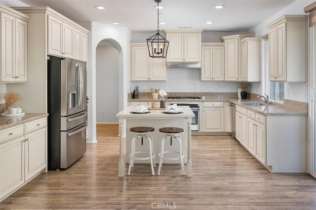 kitchen with pendant lighting, appliances with stainless steel finishes, a kitchen island, light hardwood / wood-style floors, and a kitchen bar