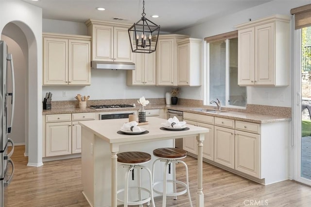 kitchen featuring sink, stainless steel appliances, a center island, decorative light fixtures, and cream cabinetry