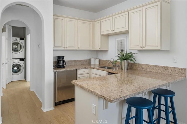 kitchen featuring stacked washer and clothes dryer, sink, light hardwood / wood-style flooring, light stone countertops, and cream cabinets