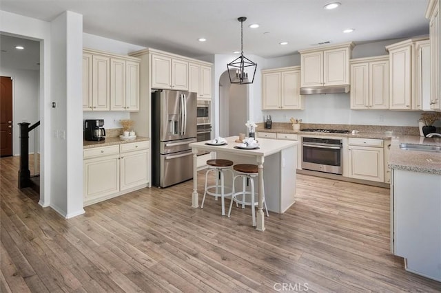 kitchen featuring a kitchen island, pendant lighting, a kitchen bar, stainless steel appliances, and cream cabinetry