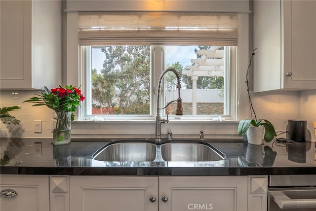 kitchen with tasteful backsplash, dark stone countertops, sink, and white cabinets