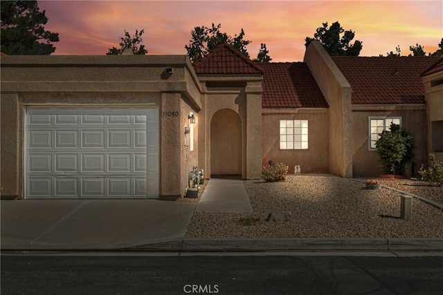 view of front facade featuring a garage, concrete driveway, a tiled roof, and stucco siding