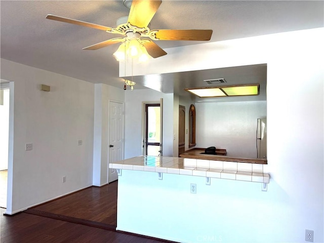 kitchen featuring tile countertops, ceiling fan, a peninsula, visible vents, and dark wood finished floors