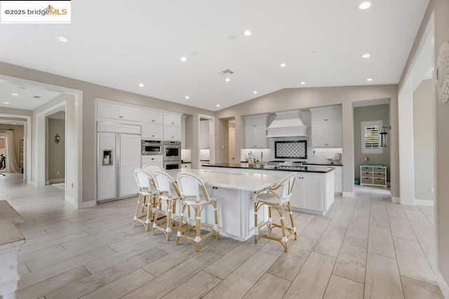 kitchen featuring a spacious island, wall chimney exhaust hood, a breakfast bar, paneled fridge, and white cabinets