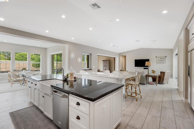 kitchen with sink, a kitchen island with sink, white cabinets, vaulted ceiling, and dark stone counters