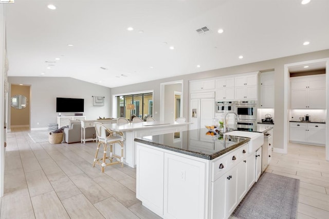 kitchen featuring white cabinetry, paneled refrigerator, dark stone counters, and a spacious island