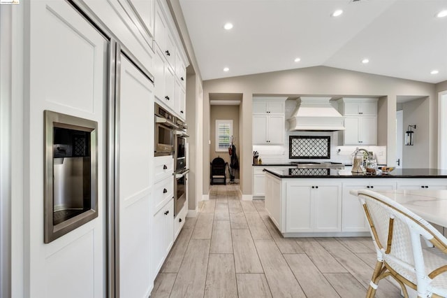 kitchen with custom exhaust hood, white cabinetry, and vaulted ceiling