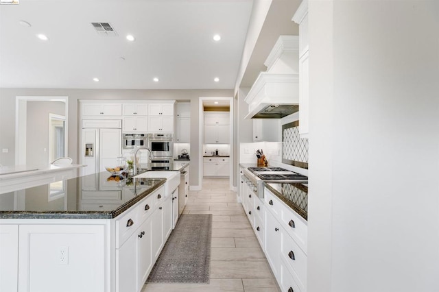 kitchen with stainless steel appliances, white cabinetry, a large island, and dark stone counters