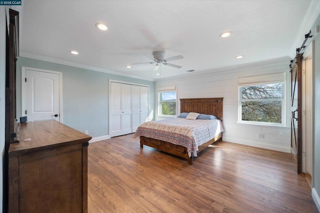 bedroom with ornamental molding, a barn door, wood-type flooring, and ceiling fan