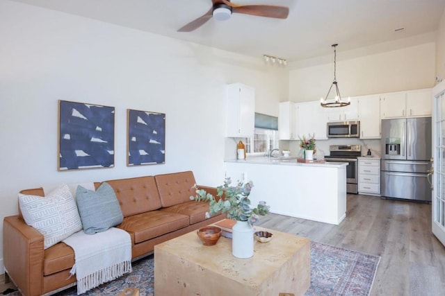 living room featuring ceiling fan with notable chandelier, high vaulted ceiling, sink, and light hardwood / wood-style flooring