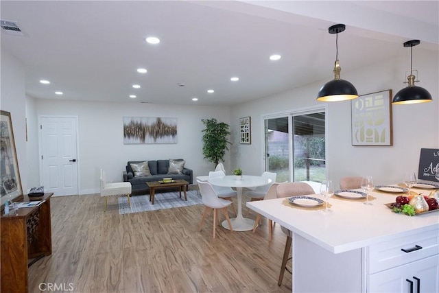 interior space with decorative light fixtures, a kitchen breakfast bar, light wood-type flooring, and white cabinets