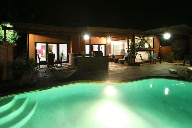 pool at night featuring outdoor lounge area and a patio