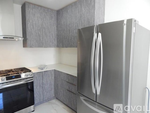 kitchen featuring wall chimney range hood, gray cabinets, and appliances with stainless steel finishes