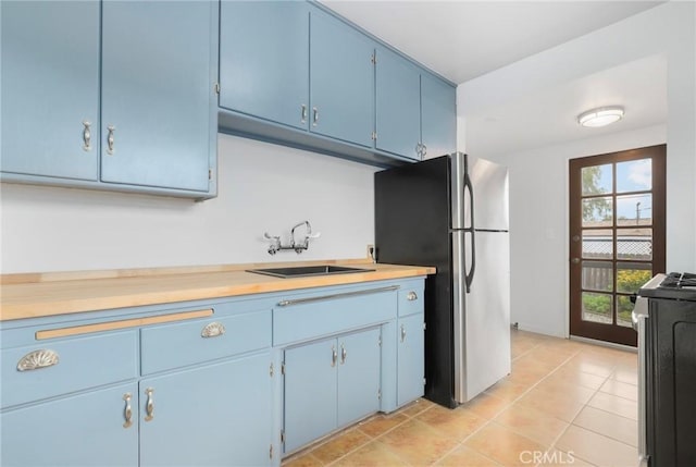 kitchen featuring sink, stainless steel refrigerator, stove, blue cabinets, and light tile patterned flooring